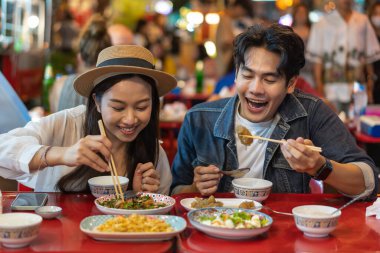 Tayland 'ın Bangkok kentindeki Çin marketinde birlikte Tayland sokak yemeği yiyen genç Asyalı çift turistler. Yemek kültürü kavramından hoşlanan insanlar.