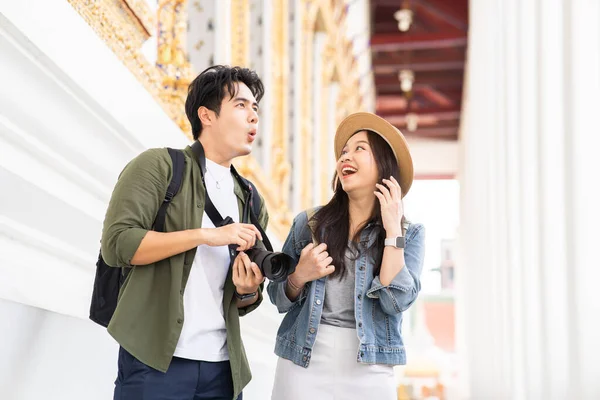 stock image Portrait of Asian man and woman couple travelers in relationship. Boyfriend taking a photo in front of buddhist temple on street in Bangkok, Thailand - people traveling photography concept
