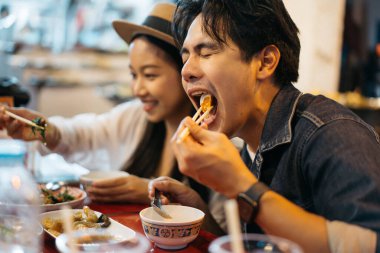 Tayland 'ın Bangkok kentindeki Çin marketinde birlikte Tayland sokak yemeği yiyen genç Asyalı çift turistler. Yemek kültürü kavramından hoşlanan insanlar.