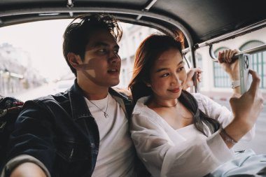 Mutlu ve neşeli genç Asyalı çift turistler tuk tuk turuna çıkıyorlar, triportör tarzı ulaşım - Tayland 'da Bangkok' ta insanlar yerel kültür kavramının tadını çıkarıyorlar.