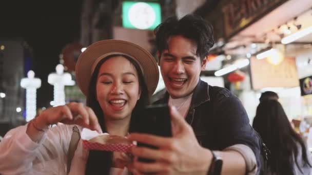 バンコクのヤワラト通りで屋台の食べ物を食べながら アジアのカップルの観光客のバックパッカーが自撮りやビデオブログを記録します — ストック動画