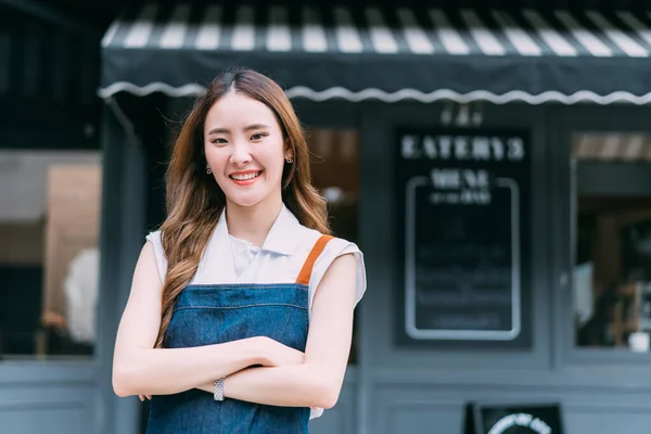 若いアジアのビジネス女性が笑顔でカフェレストランの前に腕を横切ります 腕を交差したコーヒーショップのハッピーで楽しいバリスタ — ストック写真