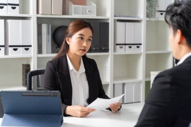 Asyalı kadın girişimci, yanında bir bilgisayar dizüstü bilgisayar varken şirket masasında genç bir iş adamını işe alıyor. Kariyer edinme konsepti