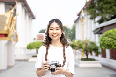 Sırt çantalı Asyalı kadın turist gülümsüyor, seyahat ediyor ve tapınak geçmişi olan Bangkok, Tayland 'da fotoğraf çekiyor.