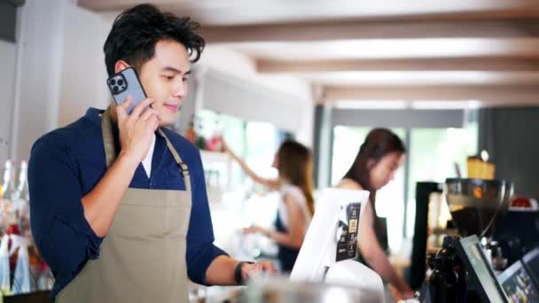 亚洲咖啡店的男性员工在咖啡店里使用平板电脑时 接受手机预购 男服务员在讲电话 家庭食品交付概念 — 图库视频影像