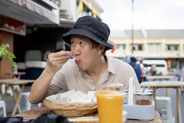 Solo travel food experience: Asian male tourist backpacker eating traditional Thai street food in Bangkok, Thailand