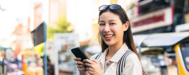 Bangkok, Tayland 'da Khaosan Yolu' ndaki açık hava pazarında gezerken gülümseyen ve cep telefonu kullanan genç bir Asyalı kadın.