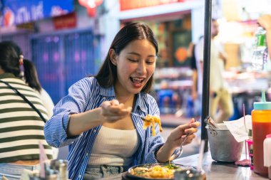Tayland, Bangkok 'ta Çin' de gece marketinde yemek yiyen genç Asyalı kadın turist. İnsanlar yemek kültürü kavramının keyfini çıkarıyorlar.