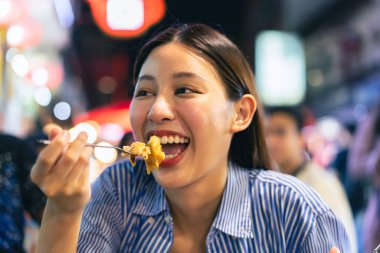 Tayland, Bangkok 'ta Çin' de gece marketinde yemek yiyen genç Asyalı kadın turist. İnsanlar yemek kültürü kavramının keyfini çıkarıyorlar.