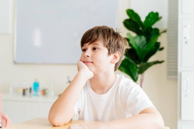 Sınıftaki çilli çocuk. Düşünüyor ve hayal kuruyor. Masasında beyaz gömlekli genç bir öğrenci, rahat ve rahat, gençliğini ve masumiyetini sergiliyor. Eğitim ve öğrenim ortamı portresi