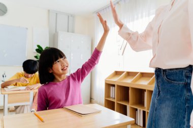 Neşeli Asyalı ilkokul öğrencisi enerjik beşlik çakarak öğretmeniyle başarıyı kutluyor.