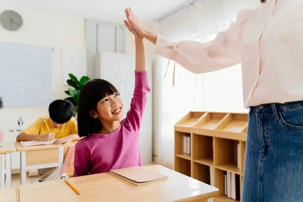 stock image Joyful Asian primary student celebrating achievement with teacher through energetic high-five