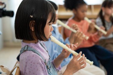 Çeşitli ilkokul öğrencileri canlı müzik sınıfında flüt çalışıyor. Genç müzisyenler ahşap rüzgâr topluluğunda işbirliği yaparak, ortak müzik deneyimi yoluyla küresel uyumu teşvik ediyorlar.