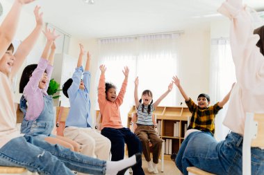 Çeşitli geçmişlere sahip heyecanlı ilkokul öğrencileri birlikte mutluluğu ifade ediyorlar. Neşeli sınıf sahnesi modern eğitimin özünü yakalıyor, birlik ve aktif katılımı vurguluyor