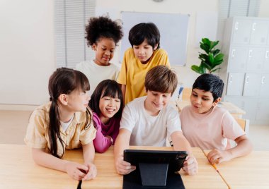 Çeşitli ilkokul öğrencileri modern sınıfta dijital tablet üzerinde işbirliği yapmaktadırlar. Çok kültürlü gruplar etkileşimli öğrenme, kapsayıcı eğitim ve teknolojik entegrasyonla ilgilenirler.