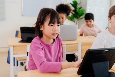 Genç Asyalı kız çeşitli ilköğretim sınıflarında tabletle meşgul oluyor. Öğrenciler dijital öğrenimi, modern eğitim tekniklerini ve okullardaki teknoloji entegrasyonunu kucaklıyor