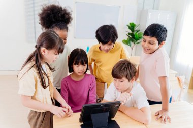 Çeşitli ilkokul öğrencileri modern sınıfta dijital tablet üzerinde işbirliği yapmaktadırlar. Çok kültürlü gruplar etkileşimli öğrenme, kapsayıcı eğitim ve teknolojik entegrasyonla ilgilenirler.