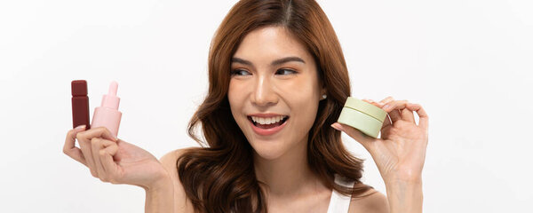 Banner of Asian woman with flowing hair and a joyful expression holds up skincare items in a well-lit, minimalist studio. She highlights various beauty products, emphasizing skincare.