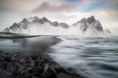 İzlanda 'daki Vestrahorn Dağı, Stokksnes plajı ve Atlantik Okyanusu ile ikonik bir yer, dalgalar geliyor, ıslak sahildeki dağın yansıması.