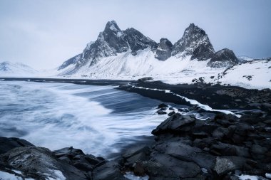 İzlanda 'nın Eystrahorn Dağı' nda fırtınalı bir kış akşamı. Dağları kaplayan kar ve Atlantik Okyanusu 'ndan gelen azgın dalgalar.