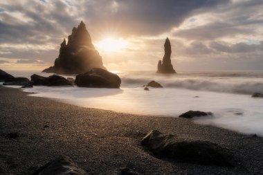Atlantik Okyanusu 'nda Reynisfjara olarak da bilinen Vik kasabası yakınlarındaki İzlanda' daki kara kum plajı, deniz yığını oluşumları, dalgalar, renkli gündoğumu, turizm beldesi