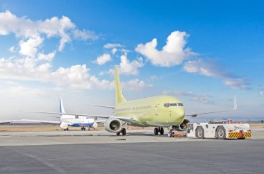 Çekici jeti havaalanındaki otoparka doğru itiyor. Arka planda başka bir uçak