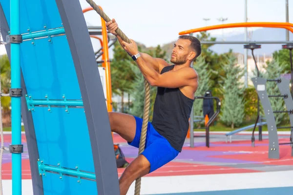Man climbs a wall with a rope. Rope climbing exercise in a fitness gym in a city park
