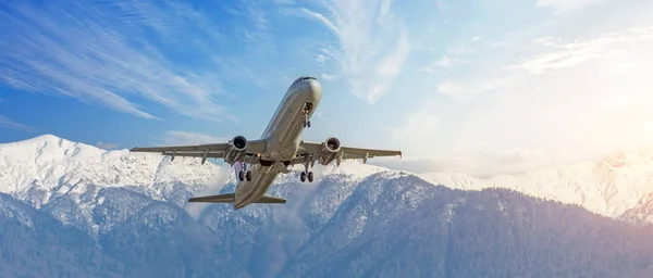 Passenger civil aircraft takes off against the backdrop of massive snow capped mountains. Panoramic wide view banner format