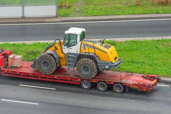 Truck with a long trailer platform for transporting heavy machinery, loaded tractor with a bucket. Highway transportation