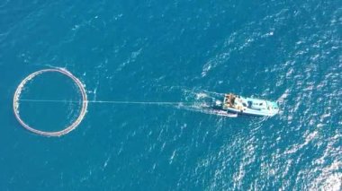 Açık deniz balık çiftliğinde balıkçı teknesi. Kafesteki balıkların tarım ve liman pazarına taşınması. Mavi deniz arka planı. Havadan üst görünüm