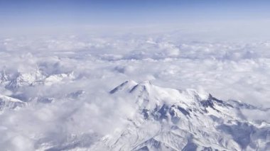 Dağ karları kış mevsiminde bir uçağın yüksekliğinden doğar. Dağ sırasının karla kaplı zirvesi bulutlarla kaplıdır.