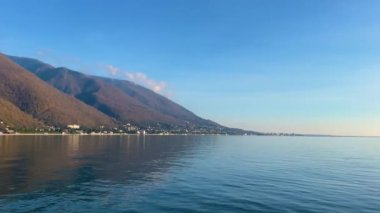 Orman ve yüksek dağlarla kaplı deniz kıyısı manzarası, dağ setinin eteğindeki küçük bir kasaba.