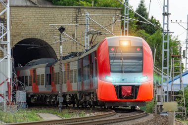 Passenger suburban train leaving the tunnel with headlights on
