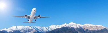 Large passenger jet airliner takes off rapidly over a mountain range against the background with a clear sky, banner wide view