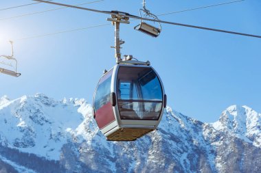 Cable car on the slopes of a ski resort with houses and a snowy peak in the distance, sunny winter day
