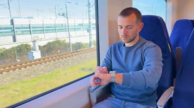 Middle aged man looks at his watch to find out what time it is on the way, outside the window is a view of bridge river nature a forest in a highland valley