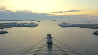 Cargo tanker with oil products sails enters the gate, the dam harbor of an industrial city port at dawn in the morning, aerial view