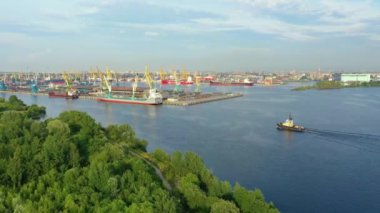 Büyük bir şehrin kargo limanından, yeşil bitki ağaçlarının üzerinden uçarak. Römorkör gemisi körfezin körfezinden kalkıyor, hava manzaralı.