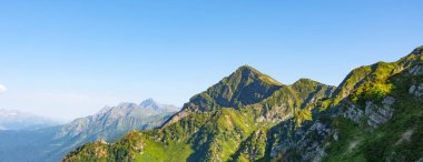 Panorama of a mountain range with shady gorges and alpine meadows on the slopes, other mountains in the distance