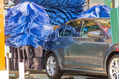 Otomatik yıkama mavi fırça devrede, gri araba temiz çıkıyor.