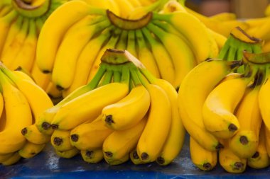 Sarı olgun muzlar, arka planda diğer meyvelerle birlikte bir market tezgahında yatar.
