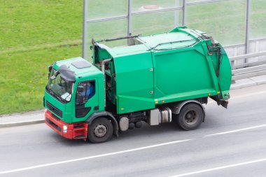 Şehrin yerleşim bölgesinde çöp toplamak için kullanılan yeşil bir kamyon yol boyunca ilerliyor.