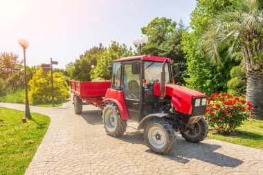 Special equipment tractor with a trailer in the city park, cleaning and care of the territory and plants clipart