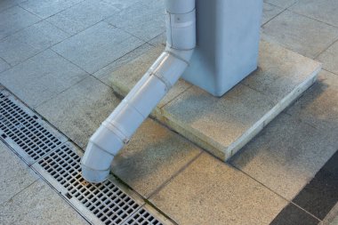 Ucunda bir lağım borusu olan metal bir boru. Metal bir beton desteğe bağlı. Burs levhalarında siyah metal bir ızgaraya doğru gidiyor.