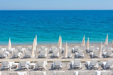 Beyaz plaj şemsiyeleri ve kumsalda güneşlenen manzaralar.