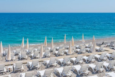 Sahilde beyaz plaj şemsiyeleri ve kumsalda güneşlenen yerler.