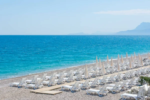 stock image Landscape coast with white beach umbrellas and sun loungers on the sand beach, against the backdrop of grief in the distance
