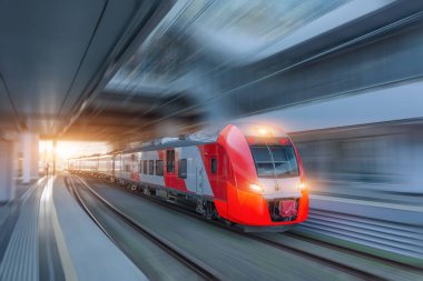Banliyö yolcusu elektrikli tren, tren istasyonundaki platformu geçerek parlak ışıkla tünele doğru hızla ilerliyor.