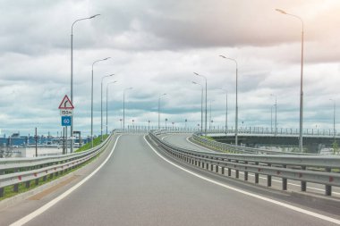 Otobanın çıkışı arabalardan arınmış, köprünün ilerisinde bir kavşak var. Yol işareti dönüş ve hız limitiyle
