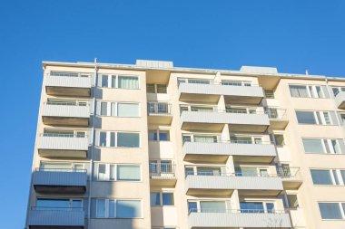 Balkonları ve pencereleri olan çok katlı beyaz beton bir bina.